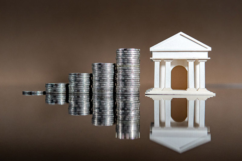 Stack of coins next to small statue of bank